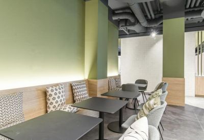 Lounge area with light green walls, wooden accents, and small black café tables with patterned seating.