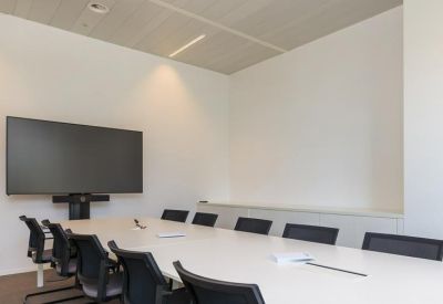 Modern meeting room featuring a large wall-mounted screen and long white conference table.
