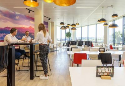 Bright coworking area with white tables, red accent chairs, and a scenic mountain wall mural.