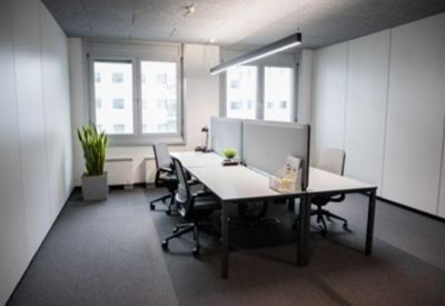 Bright, modern open-plan office with white desks, grey dividers, and a potted plant.