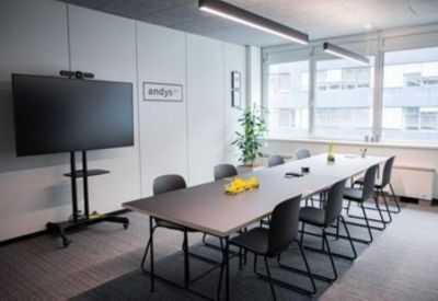 Professional meeting room with a large table, black chairs, and a wall-mounted screen.