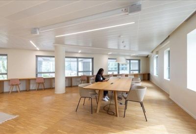 Spacious coworking area with long wooden tables, natural light, and individual workstations.