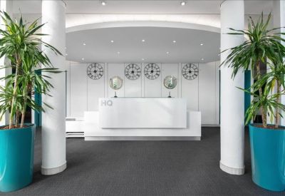 Sleek white reception desk flanked by white columns and tall potted palms.