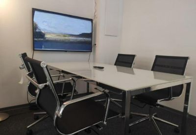 Modern meeting room with a white table, black chairs, and a wall-mounted display screen.