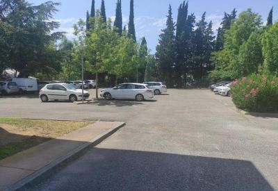 Outdoor parking area surrounded by tall cypress trees and green landscaping.