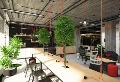 Lounge area featuring long wooden tables, vibrant green plants, and red accent seating under an industrial ceiling.