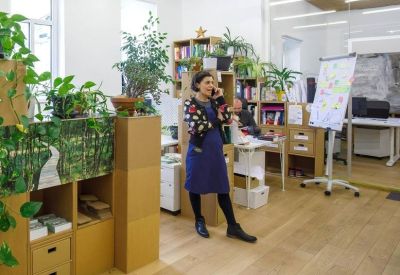 Bright office space with wooden floors, indoor plants, and a woman on a phone call.