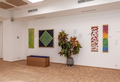 Clean white corridor featuring colorful textile art and potted plants.