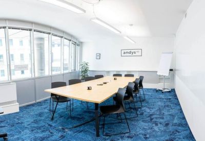 Professional meeting room with a large light wood table, blue carpet, and floor-to-ceiling windows.