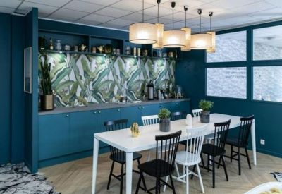Modern communal kitchen and dining area featuring deep teal walls and leafy tropical backsplash.