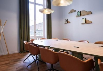 Sun-drenched meeting room with a large oval wooden table and tan leather chairs.