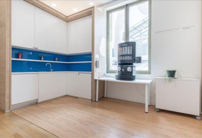 Minimalist communal kitchen with white cabinetry and a blue tiled backsplash.