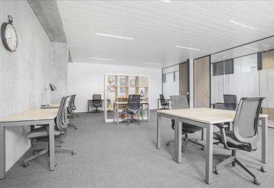Bright open-plan coworking space with several white desks and ergonomic grey chairs.