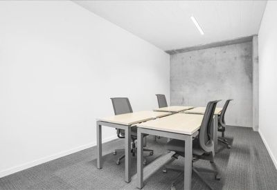 Private four-person office suite with minimalist white desks and a concrete feature wall.