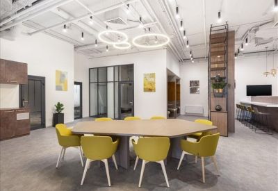 Spacious coworking area with a geometric table, yellow chairs, and modern ring lighting.