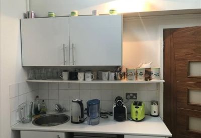 Compact office kitchen with white cabinets and various small appliances.