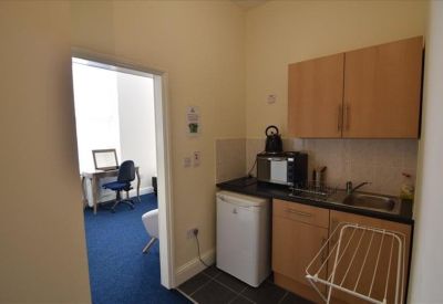 View from a kitchen area looking through a doorway into a blue-carpeted office.