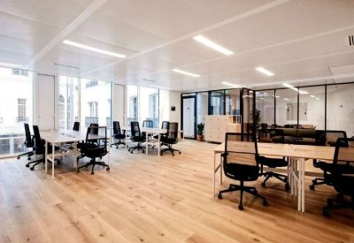 Bright open-plan office with white desks, ergonomic black chairs, and large windows.