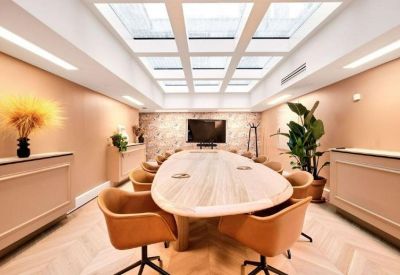 Modern meeting room with a large oval wooden table, tan leather chairs, and a glass-paneled ceiling.