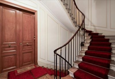 Grand entryway with a sweeping staircase, ornate wood doors, and a plush red carpet.