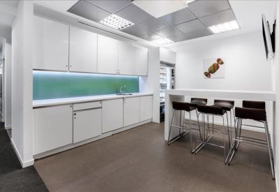 Modern office kitchen with white cabinetry, green backsplash, and high-top seating.