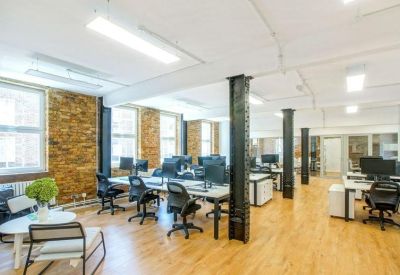 Open-plan office space with rows of desks, black swivel chairs, and industrial columns.
