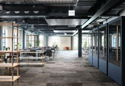 Open-plan office space with rows of white desks and black ergonomic chairs.