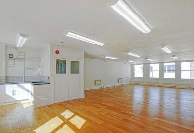 Clean communal kitchen space connected to a large open-plan area with light wood floors.