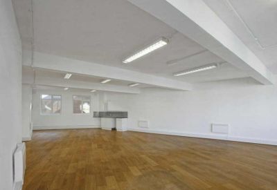 Large empty office floor with polished wood flooring and overhead fluorescent lighting.
