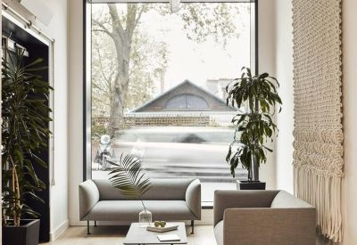 Reception area with light grey sofas, indoor plants, and a large window overlooking the street.