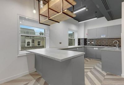 Modern communal kitchen with a grey island, wood shelving, and chevron flooring.