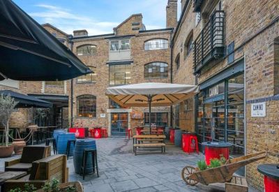 Outdoor seating area with umbrellas and colorful red barrels in a brick courtyard.