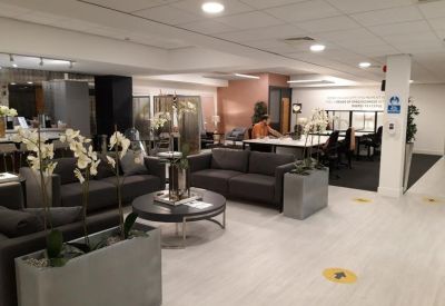 Spacious communal lounge with dark grey sofas and indoor plants.