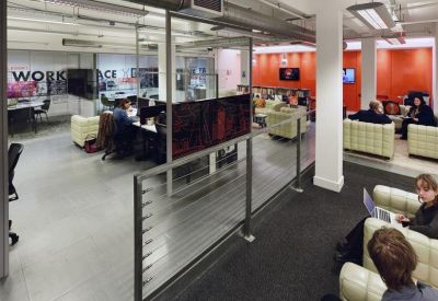 Coworking lounge area with quilted cream sofas, an orange feature wall, and a view into a kitchen.