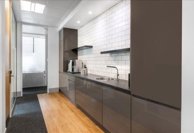 Sleek kitchen area with dark cabinetry, white tiled backsplash, and wooden flooring.
