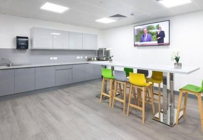 Bright communal kitchen and breakout area featuring high wooden stools with colorful seats.