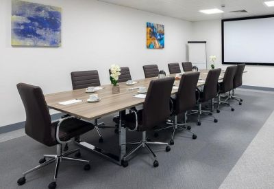 Spacious meeting room featuring a long wooden table, dark executive chairs, and colorful wall art.
