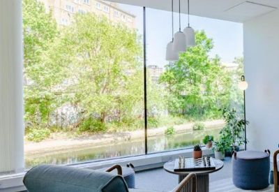 Bright communal lounge area with a blue armchair, board games, and views of a canal.