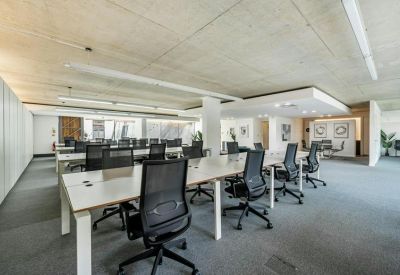 Spacious open-plan workspace with rows of modern white desks and black mesh ergonomic chairs.