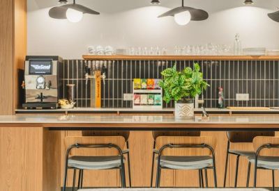 Sleek office kitchenette and coffee bar featuring black tile backsplash, wooden cabinetry, and pendant lighting.
