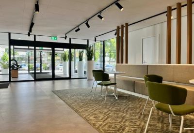 Building lobby lounge area with green armchairs, a geometric patterned rug, and wood-slat room dividers.