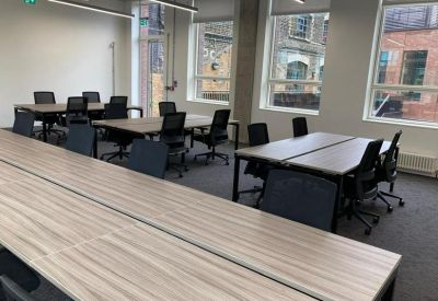 Bright workspace featuring several wooden desks with ergonomic black chairs.