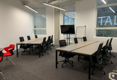 Meeting room with two long tables, black chairs, and a presentation screen.