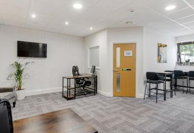 Bright common area with a grey armchair, wooden desk, and high-stool seating area.