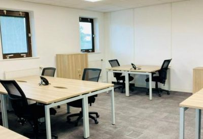 Modern office space with several light wood desks and black ergonomic mesh chairs.