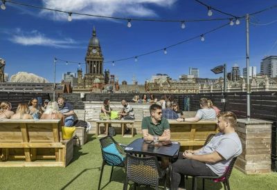 Sunny rooftop terrace with artificial grass, wooden benches, and city views.
