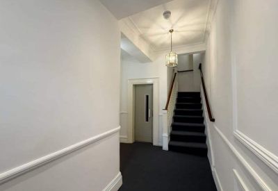 White walled hallway featuring a black carpeted staircase and an elevator door.