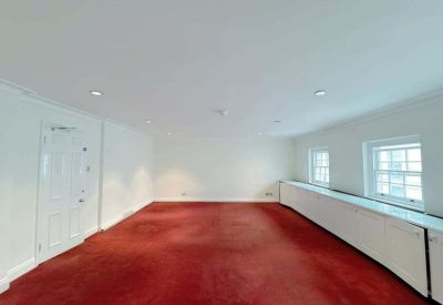 Spacious empty office room with red carpet and large windows providing natural light.