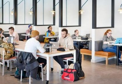 Bright open-plan workspace with multiple people working at long white tables near glass-partitioned booths.
