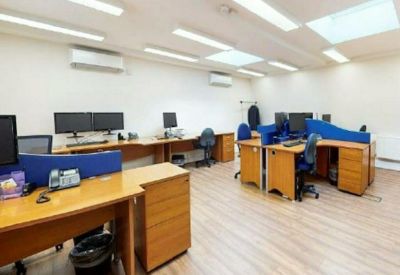 Bright open-plan office space with wooden desks, blue privacy screens, and skylights.